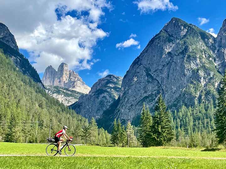 A biker biking across a field with large mountains in the distance.